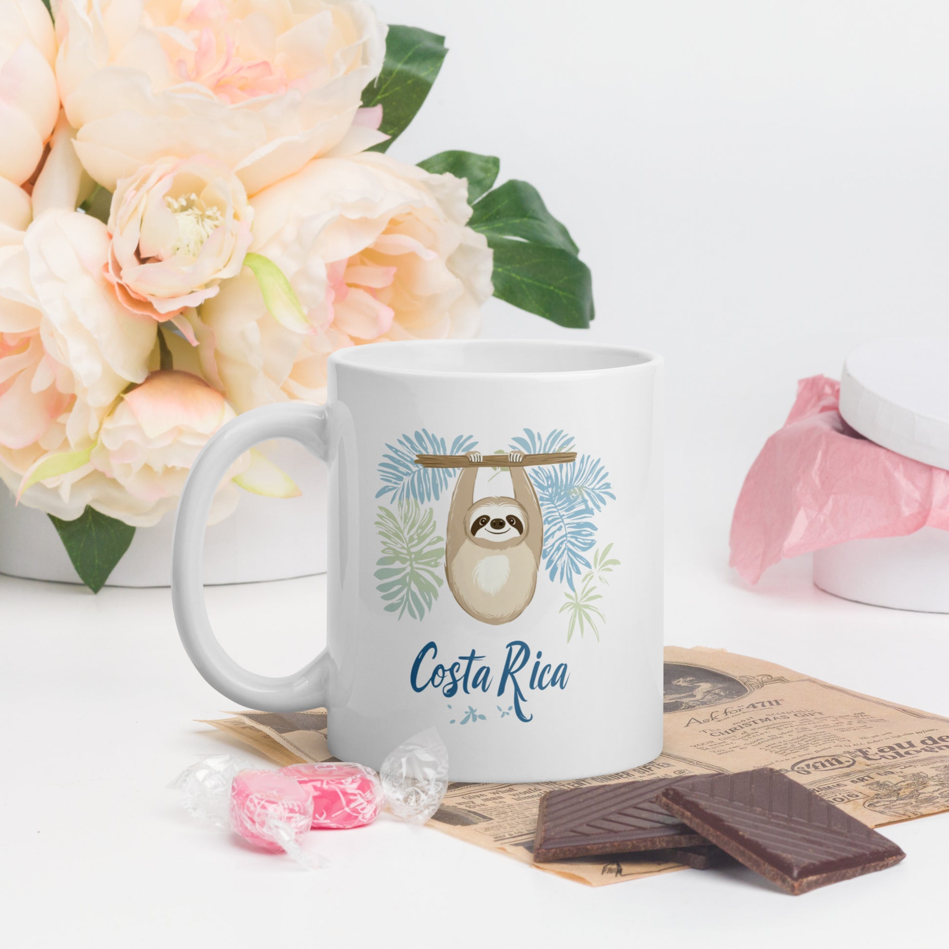 Decorative coffee mug featuring a cute beige sloth hanging from a branch surrounded by light blue and mint green palm leaves, with 'Costa Rica' written in flowing blue script below