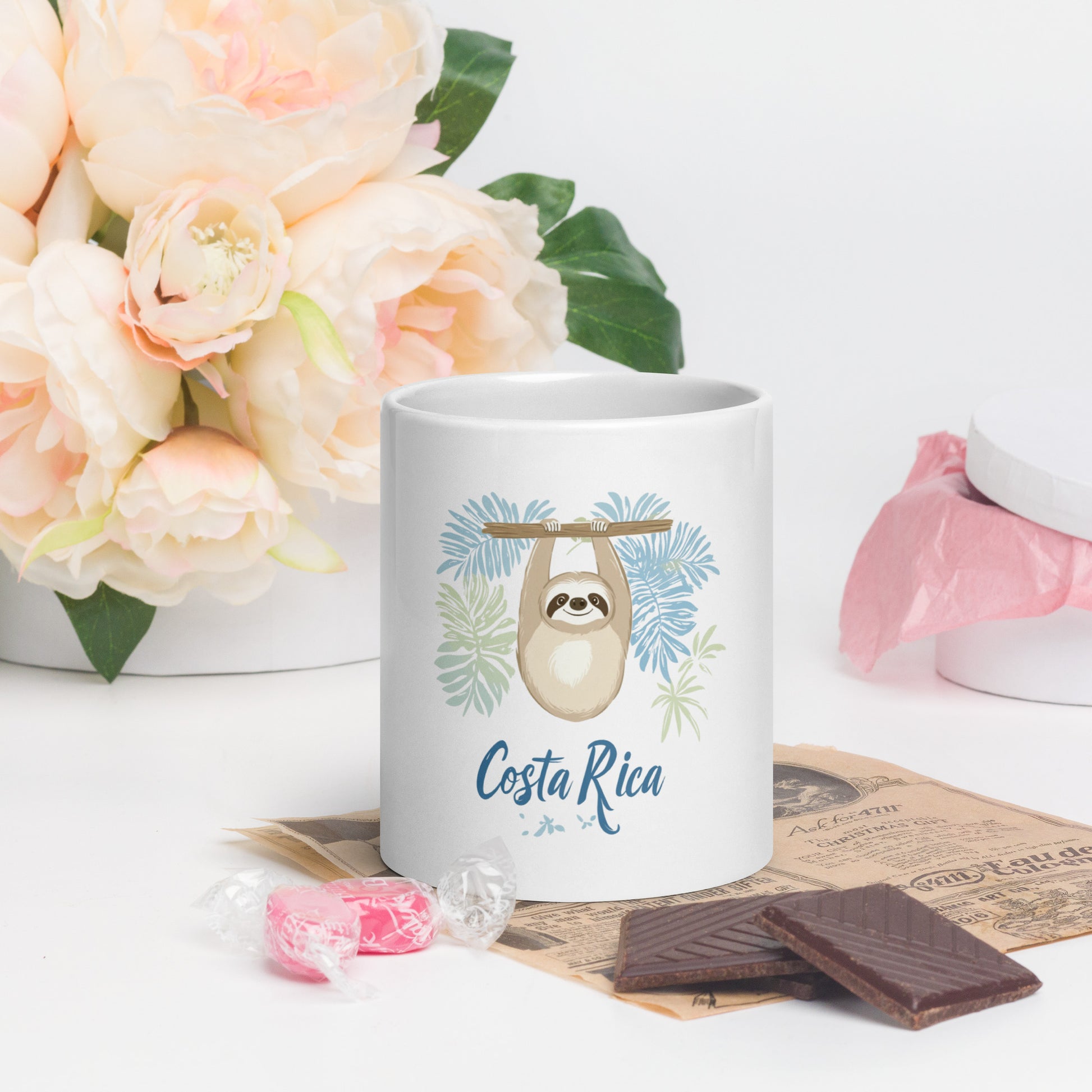 Decorative coffee mug featuring a cute beige sloth hanging from a branch surrounded by light blue and mint green palm leaves, with 'Costa Rica' written in flowing blue script below